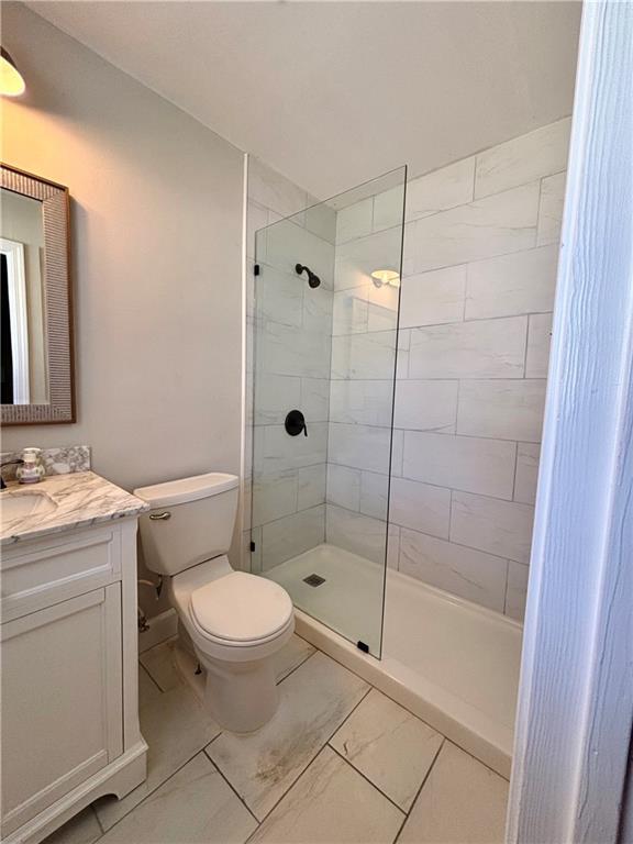 bathroom with marble finish floor, vanity, walk in shower, and toilet