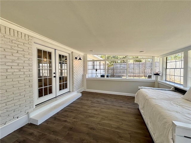 unfurnished bedroom with brick wall, french doors, multiple windows, and dark wood finished floors