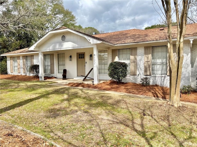 single story home featuring a front yard, covered porch, brick siding, and roof with shingles