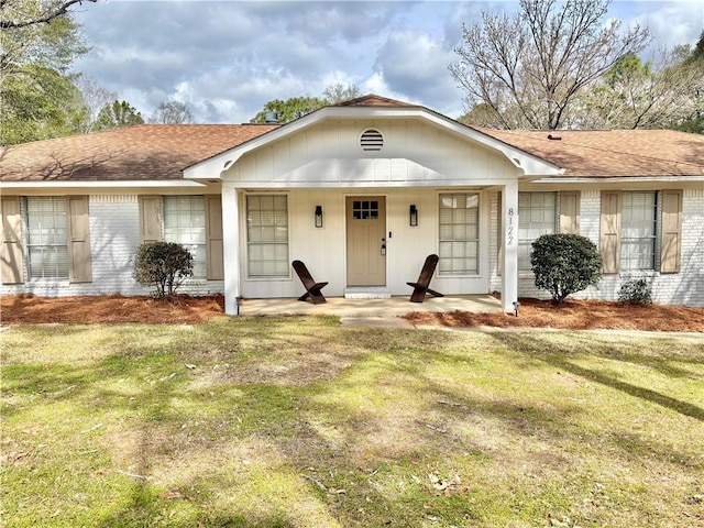 ranch-style house with covered porch, roof with shingles, a front lawn, and brick siding