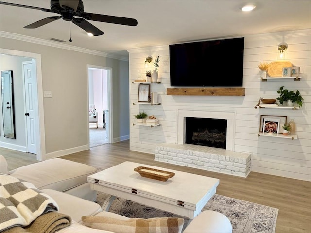 living area featuring crown molding, a brick fireplace, ceiling fan, wood finished floors, and baseboards