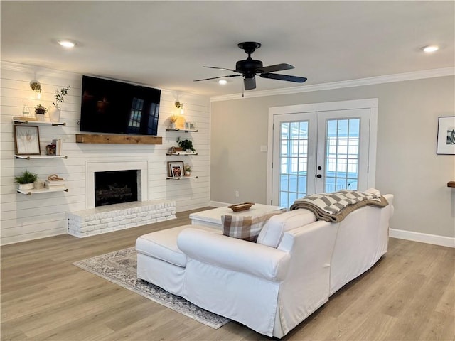 living area featuring baseboards, ornamental molding, french doors, light wood-type flooring, and a brick fireplace