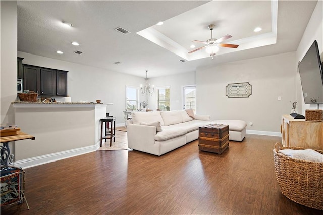 living room featuring ceiling fan with notable chandelier, dark hardwood / wood-style floors, and a tray ceiling