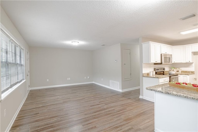 kitchen with a textured ceiling, light hardwood / wood-style flooring, appliances with stainless steel finishes, white cabinetry, and light stone counters