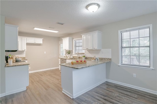 kitchen featuring a wealth of natural light, kitchen peninsula, light stone countertops, and light hardwood / wood-style floors