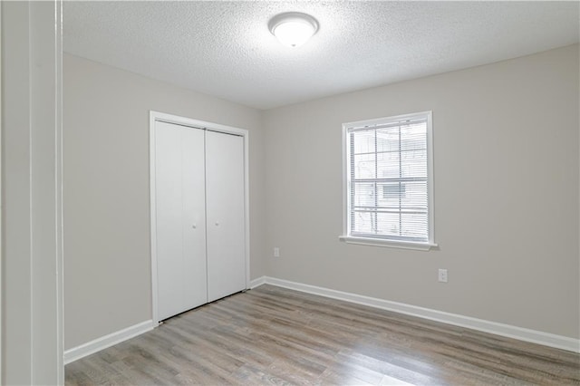 unfurnished bedroom featuring a closet, a textured ceiling, and light hardwood / wood-style flooring