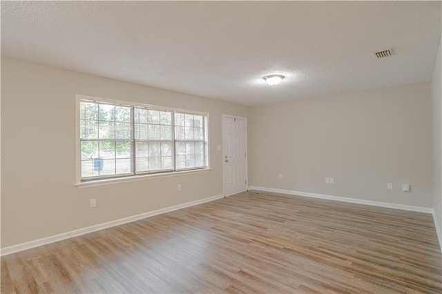 empty room with a textured ceiling and light hardwood / wood-style flooring