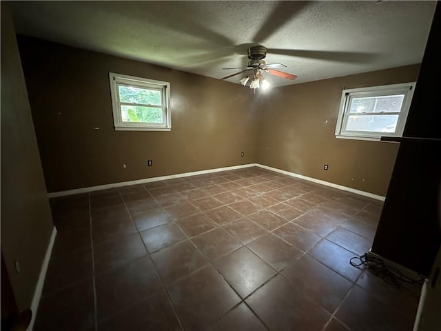 empty room featuring dark tile patterned flooring, ceiling fan, and a textured ceiling