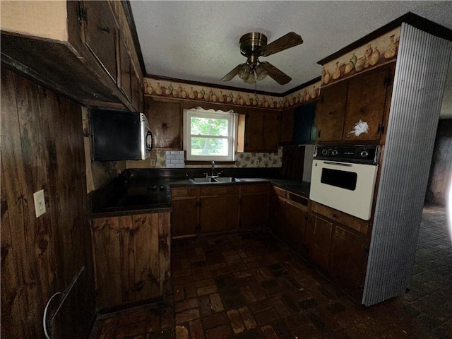 kitchen featuring backsplash, white oven, dark brown cabinetry, ceiling fan, and sink