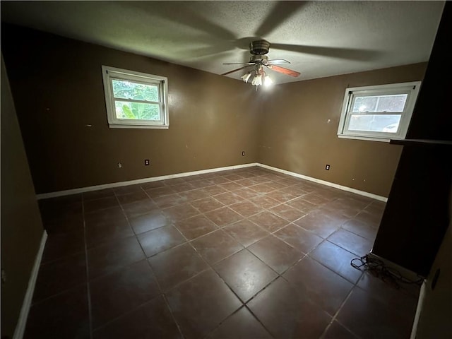 spare room featuring ceiling fan, dark tile patterned flooring, and a textured ceiling