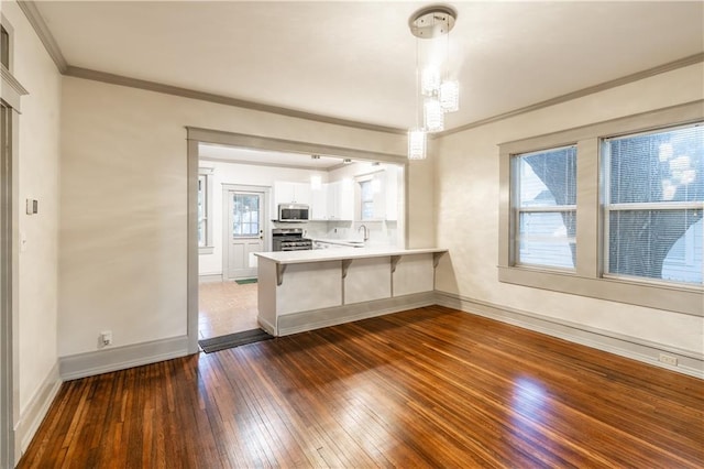 kitchen with kitchen peninsula, appliances with stainless steel finishes, dark wood-type flooring, white cabinets, and hanging light fixtures