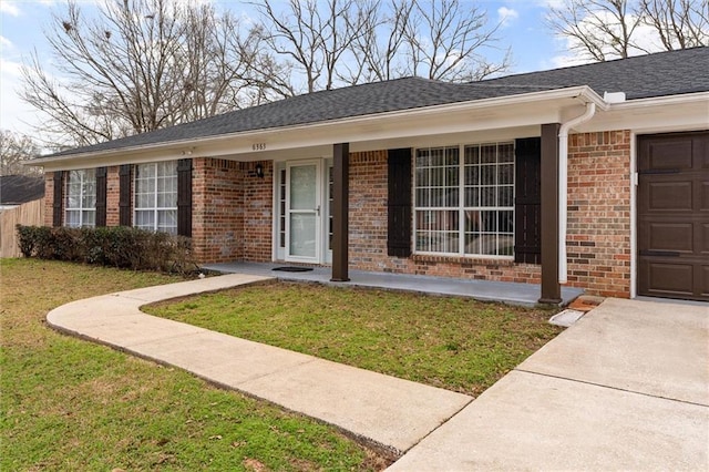 view of exterior entry with a garage, brick siding, a yard, and roof with shingles