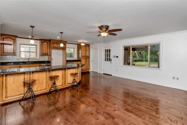 kitchen featuring dark wood-type flooring, healthy amount of natural light, dark stone counters, a ceiling fan, and ornamental molding