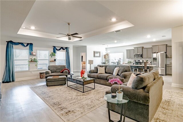 living area featuring crown molding, a wealth of natural light, a raised ceiling, and light wood-style floors
