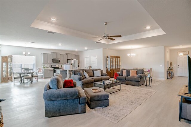 living area with ceiling fan with notable chandelier, a tray ceiling, and light wood finished floors