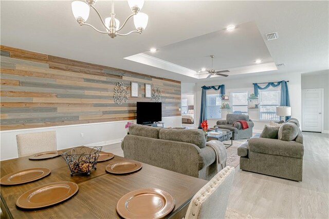 dining space with ceiling fan with notable chandelier, baseboards, wood finished floors, a tray ceiling, and visible vents