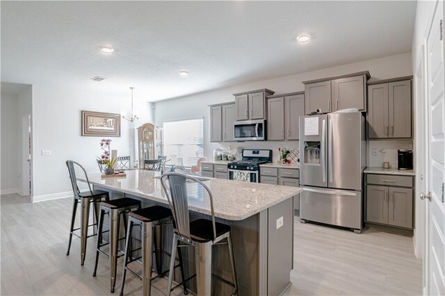 kitchen with appliances with stainless steel finishes, gray cabinets, a breakfast bar area, and an island with sink