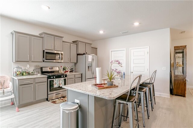 kitchen with a breakfast bar, visible vents, a kitchen island with sink, stainless steel appliances, and gray cabinetry