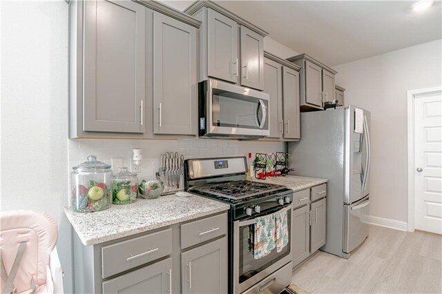 kitchen with light wood-style flooring, appliances with stainless steel finishes, gray cabinetry, and tasteful backsplash