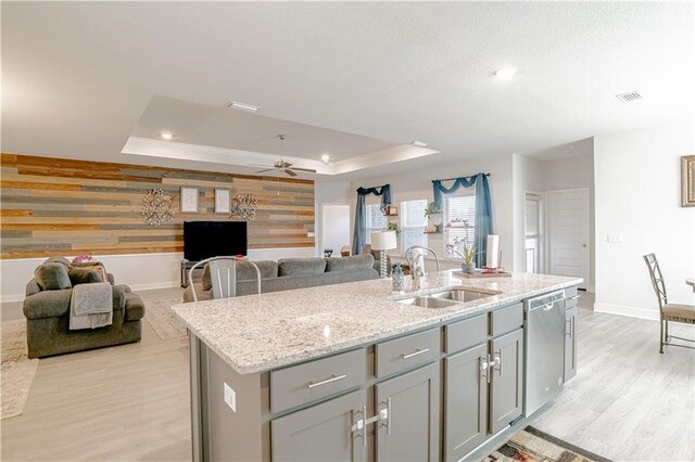 kitchen featuring gray cabinets, stainless steel dishwasher, a sink, a raised ceiling, and baseboards
