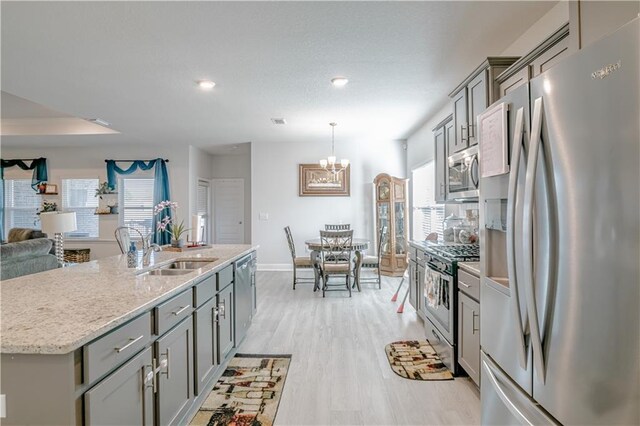 kitchen featuring open floor plan, light wood-type flooring, gray cabinets, a sink, and stainless steel appliances