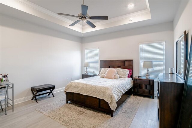 bedroom with a tray ceiling, ornamental molding, baseboards, and light wood finished floors