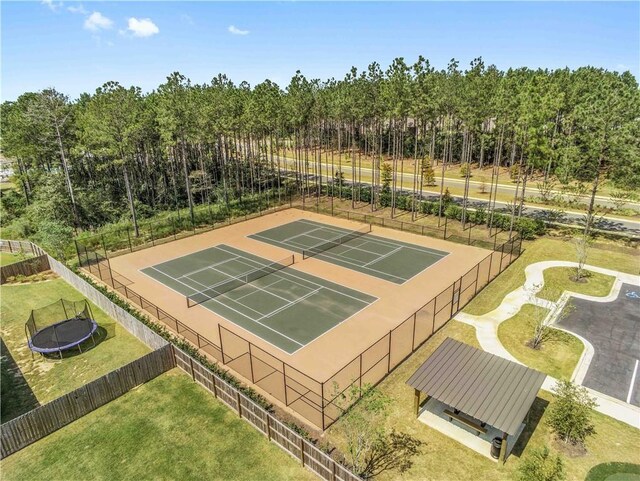 view of sport court with fence, a trampoline, and a yard
