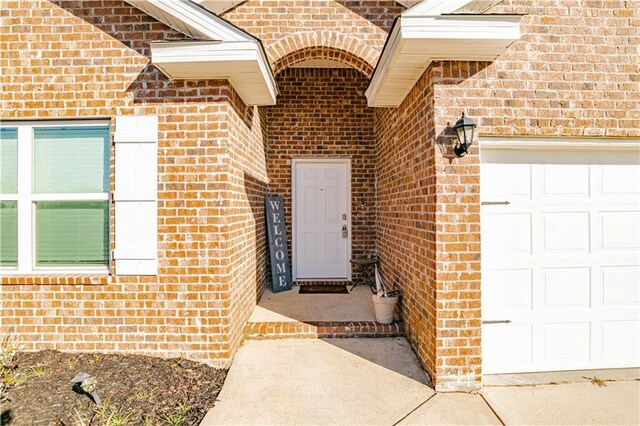 doorway to property featuring an attached garage and brick siding