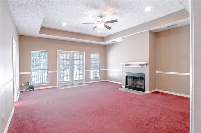 unfurnished living room with a textured ceiling, a tray ceiling, ceiling fan, and light colored carpet