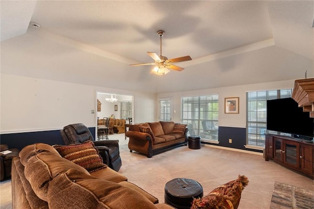 living room with vaulted ceiling, light colored carpet, a tray ceiling, and ceiling fan with notable chandelier
