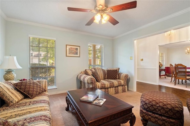 living room with baseboards, ornamental molding, carpet, and ceiling fan with notable chandelier