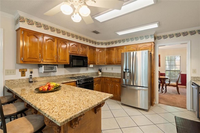 kitchen featuring brown cabinets, ceiling fan, a peninsula, visible vents, and black appliances