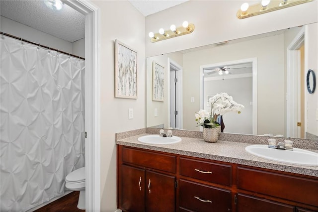 full bath featuring a sink, a textured ceiling, toilet, and double vanity