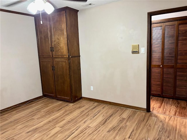 unfurnished bedroom with ceiling fan, visible vents, light wood-type flooring, baseboards, and a closet