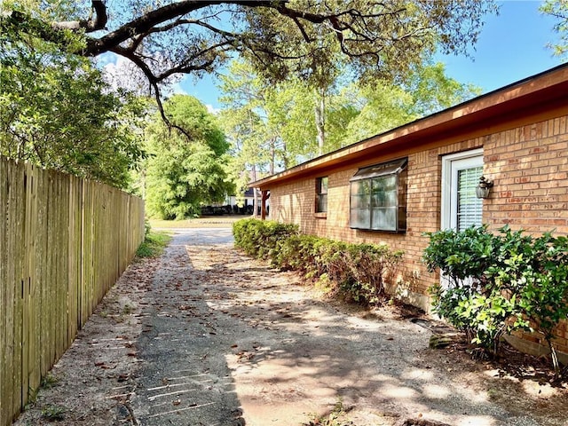 view of side of property featuring brick siding, fence, and driveway