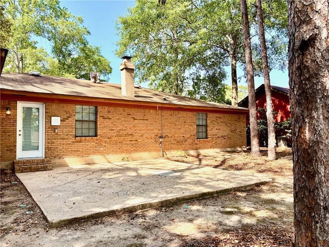 back of property featuring entry steps, a chimney, a patio area, and brick siding