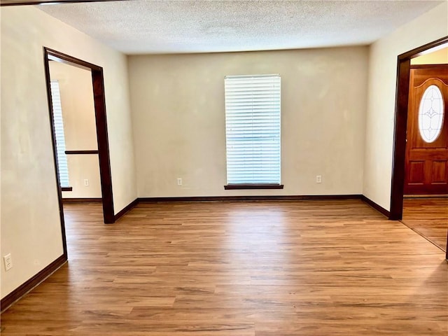 entryway featuring baseboards, light wood finished floors, and a textured ceiling