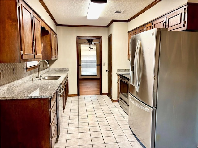 kitchen with a textured ceiling, crown molding, a sink, light tile patterned floors, and stainless steel appliances