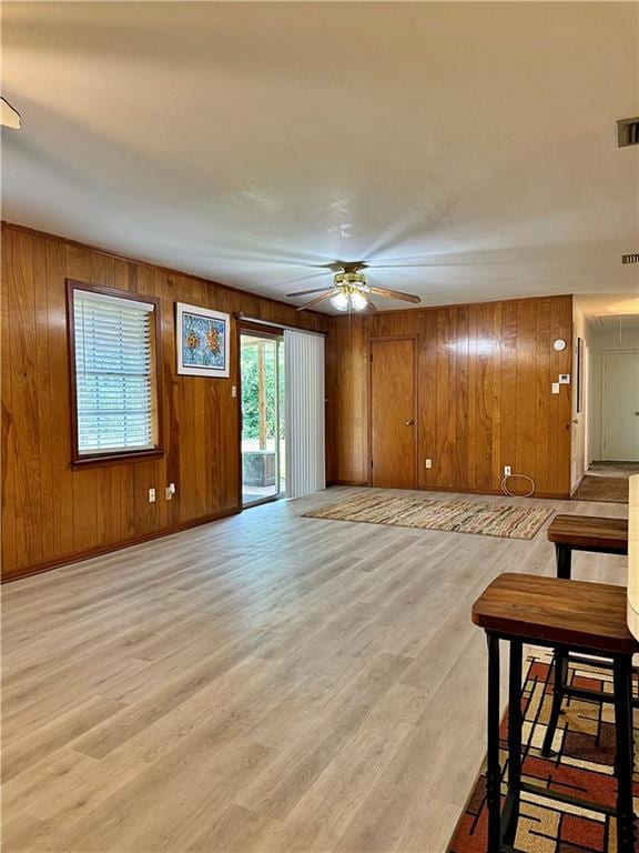 unfurnished living room with ceiling fan, wood walls, and light wood-type flooring