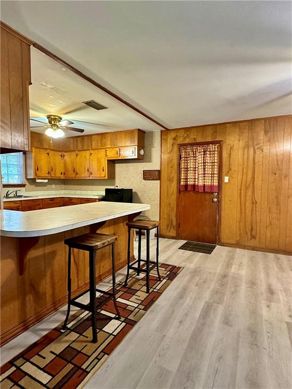 kitchen featuring light wood-type flooring, kitchen peninsula, ceiling fan, wooden walls, and a breakfast bar