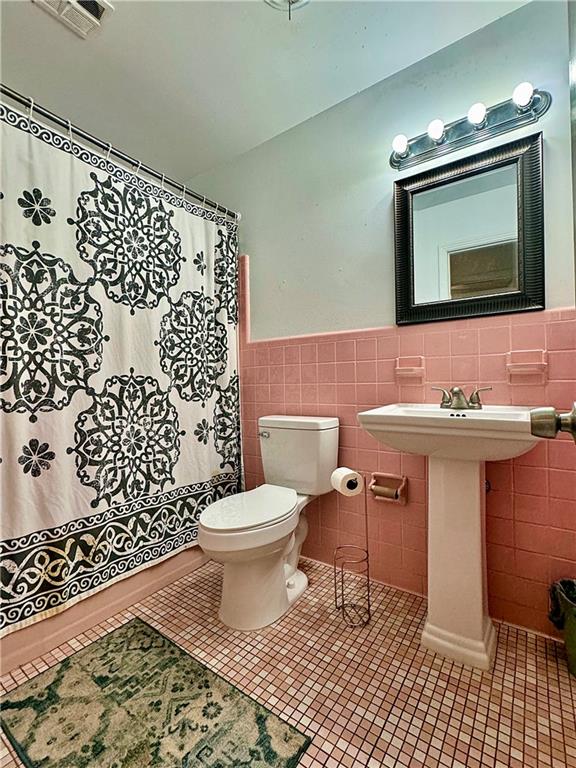 bathroom with toilet, curtained shower, tile patterned floors, and tile walls