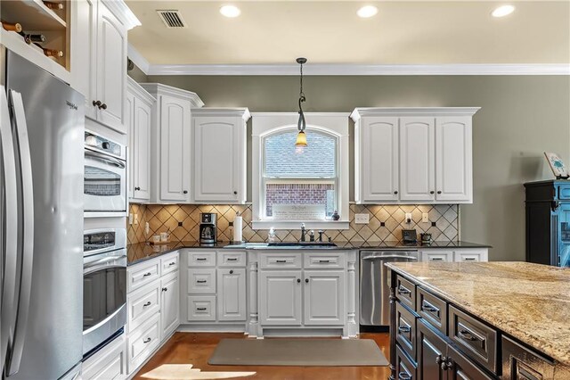 kitchen featuring stainless steel appliances, dark stone counters, crown molding, white cabinetry, and decorative light fixtures