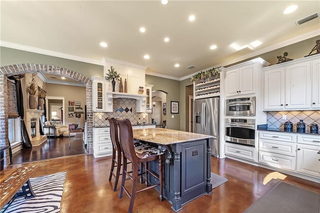 kitchen featuring decorative backsplash, white cabinets, appliances with stainless steel finishes, a kitchen bar, and a center island