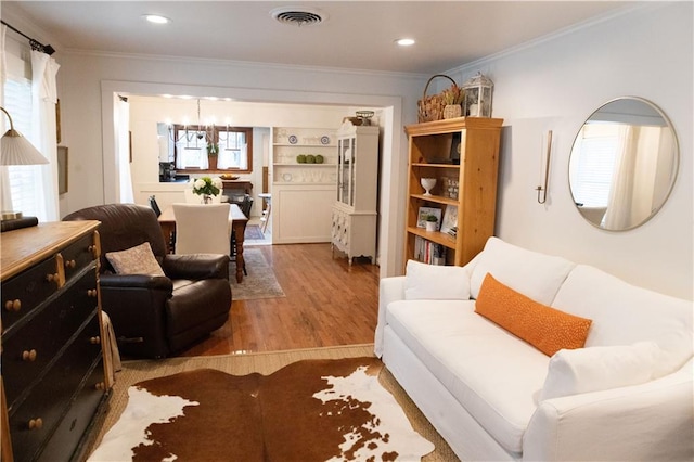 living room with ornamental molding, an inviting chandelier, and light wood-type flooring