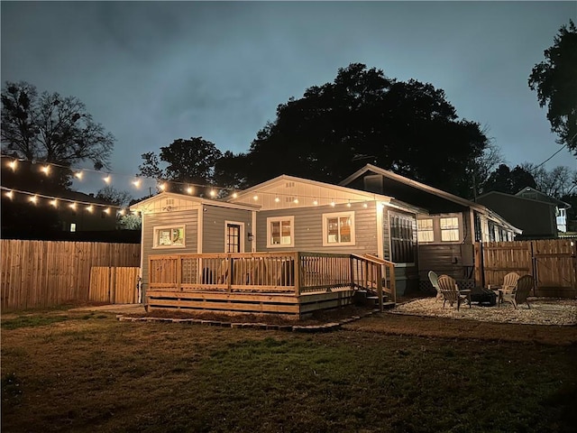 back of house featuring a wooden deck, a lawn, and a fire pit