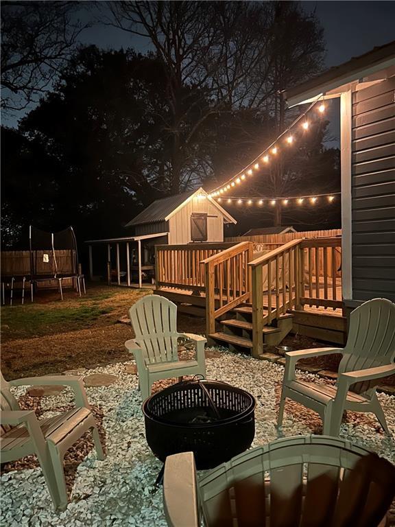 patio at night with a deck, a trampoline, and a fire pit