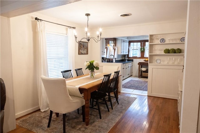 dining space featuring hardwood / wood-style flooring, ornamental molding, sink, and an inviting chandelier