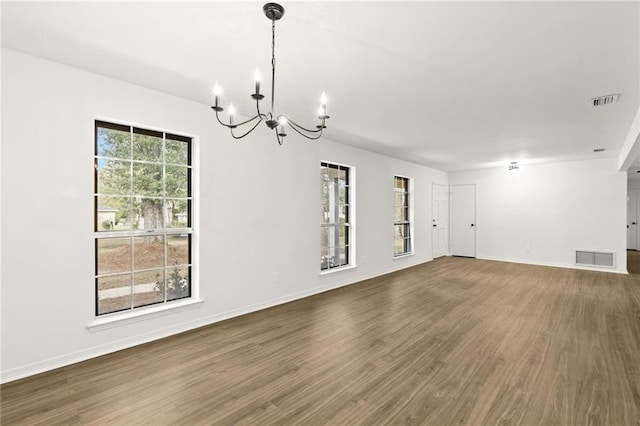 empty room with a notable chandelier, dark hardwood / wood-style flooring, and a wealth of natural light