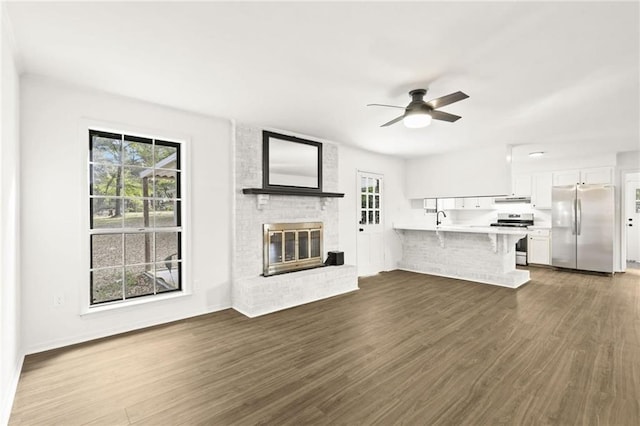 unfurnished living room featuring a brick fireplace, a wealth of natural light, and dark hardwood / wood-style floors