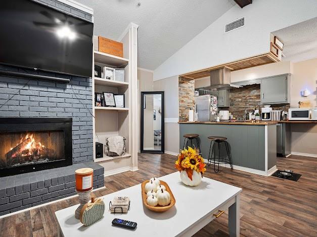 living room featuring a brick fireplace, dark hardwood / wood-style flooring, and vaulted ceiling